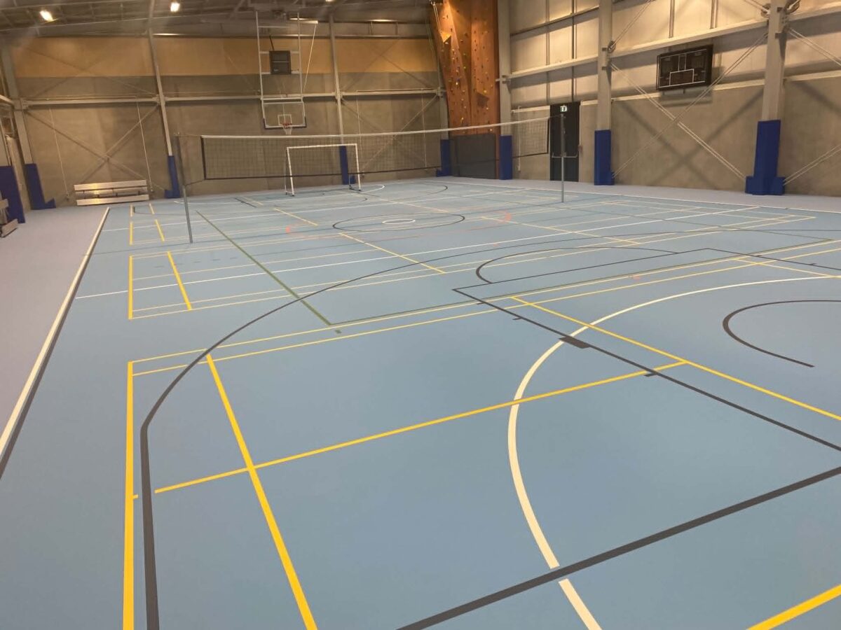 Grey-blue Herculan MF 7+2 synthetic court at Kuranui College with yellow, white and dark grey line marking, volleyball nets and blue padded posts