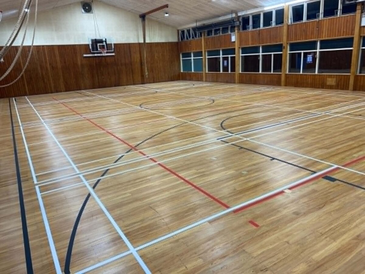 Maple timber court at Tauranga Girls College with freshly applied white, red and black line marking, dark timber panelled walls and high windows